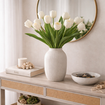 White tulips in a vase on a wooden console table with decor items.