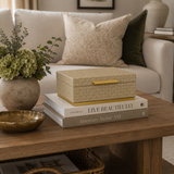 Decorative box on books with a plant and bowl on a wooden table in a living room.
