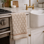 Beige towel with white floral pattern hanging on a kitchen cabinet handle.