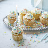 Cupcakes with white frosting and colorful sprinkles on a silver platter with a number 6 candle.
