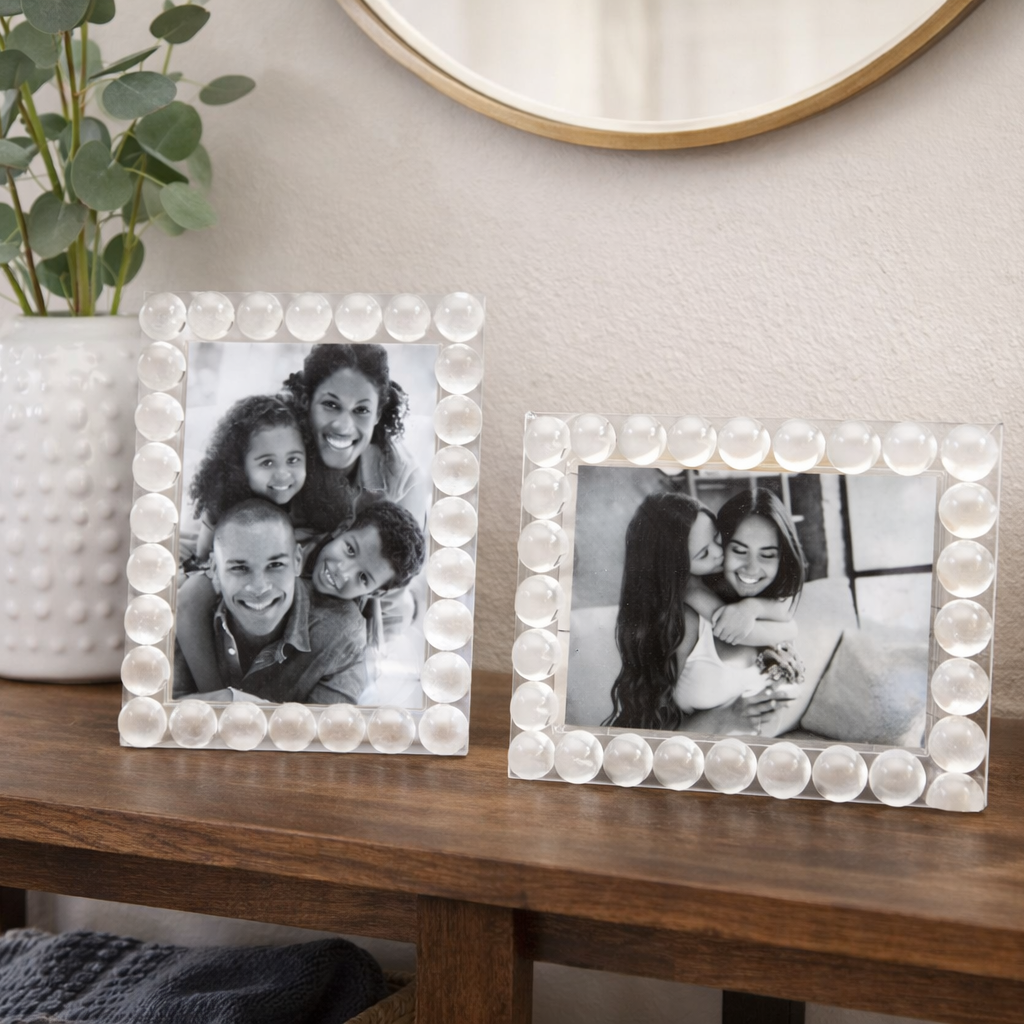 Two decorative picture frames on a wooden surface with a plant and basket in the background.