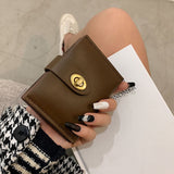 Brown leather wallet with gold clasp held by a person wearing a black and white patterned sleeve.
