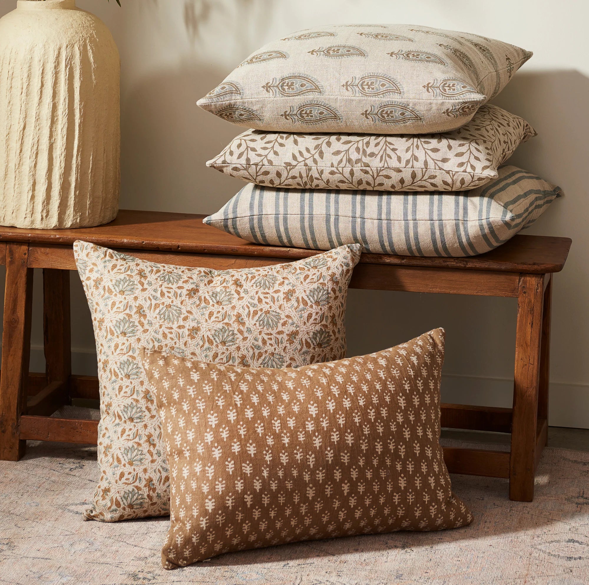 Patterned pillows on a wooden bench against a neutral wall.