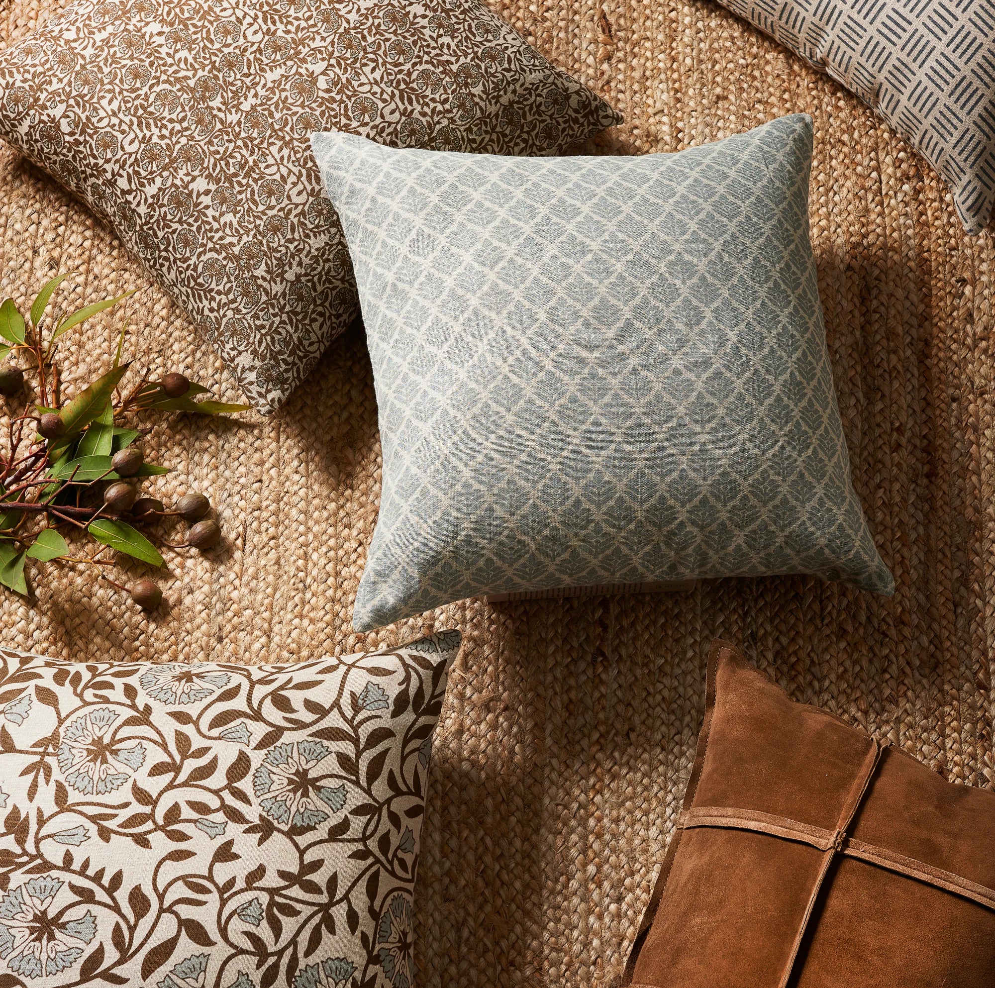 Patterned cushions on a textured surface with a plant and leather item.