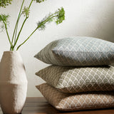 Stack of patterned pillows with a vase containing greenery on a neutral background
