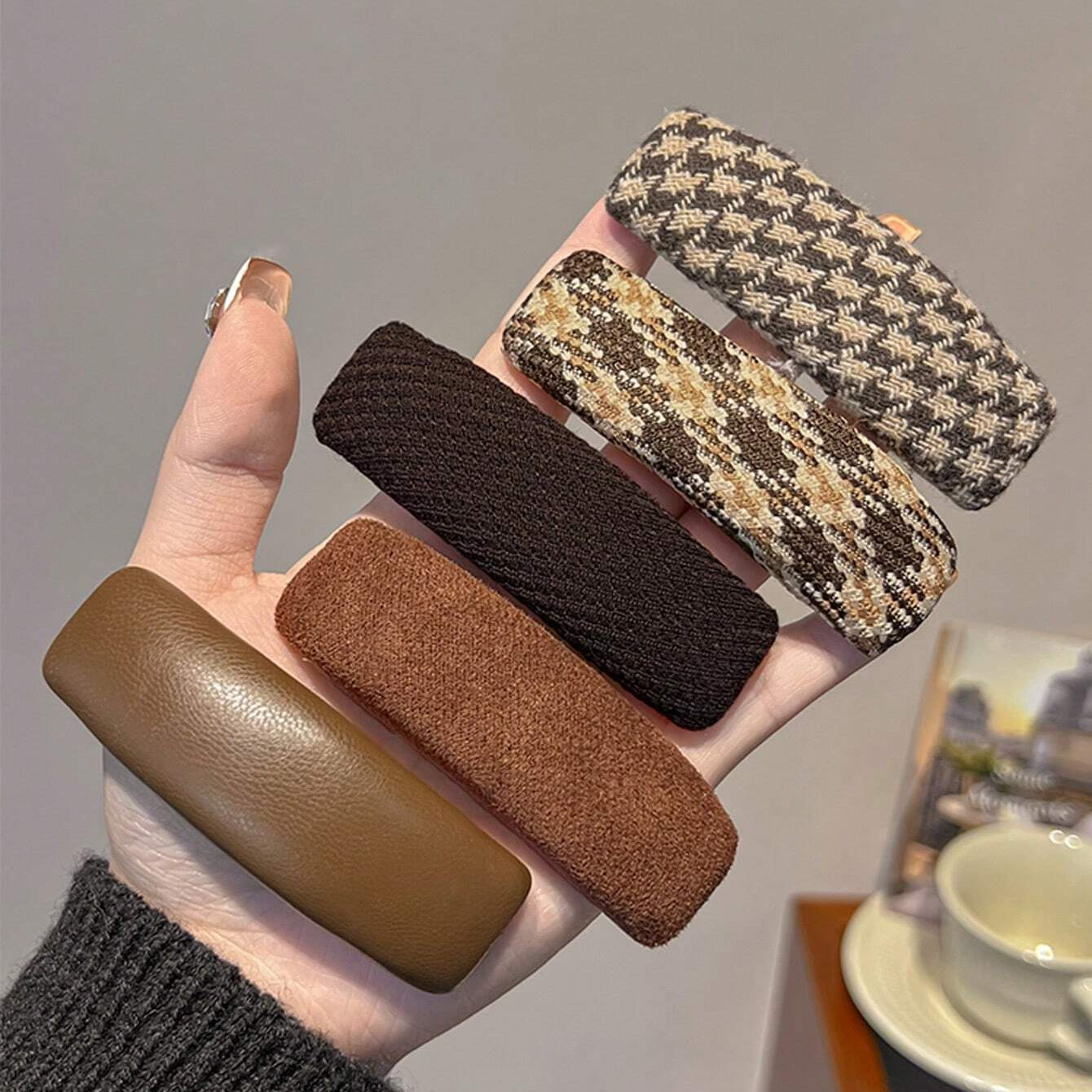 Hand holding five textured hair clips in various colors against a neutral background