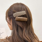 Woman with long brown hair wearing a houndstooth patterned hair clip.