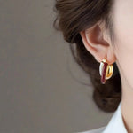 Close-up of a person wearing gold and burgundy hoop earrings against a neutral background.
