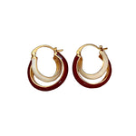 Pair of gold hoop earrings with red and white accents on a beige fabric background