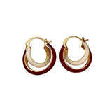 Pair of gold hoop earrings with red and white accents on a beige fabric background