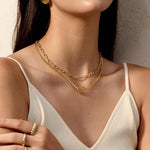 Woman wearing a gold necklace and ring with a neutral background