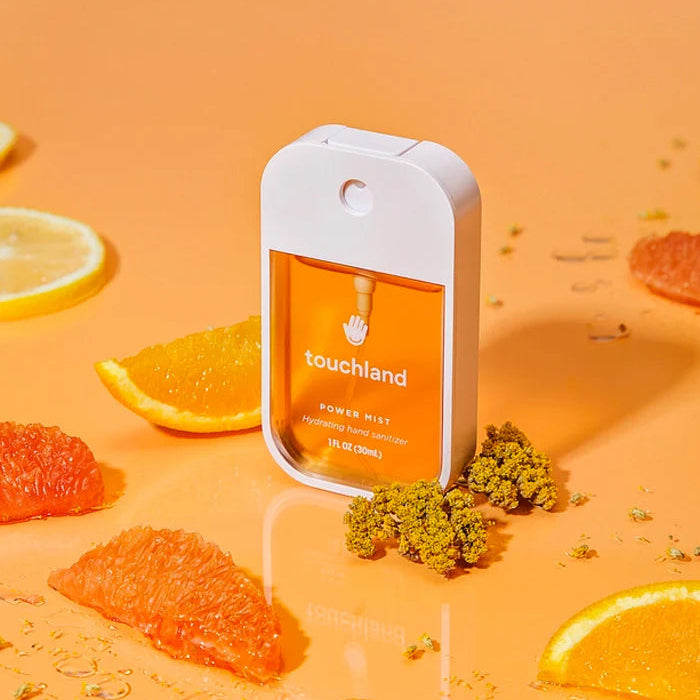Touchland hand sanitizer bottle with orange slices and leaves on an orange background