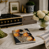 Book titled 'Love and South' on a kitchen counter with flowers and a bowl of artichokes.