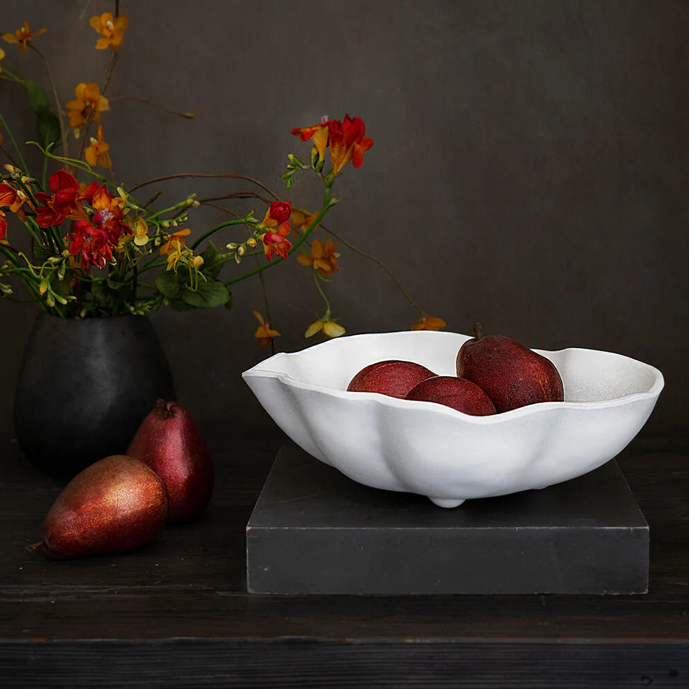 beatriz ball medium vida nube bowl with red fruits on a dark surface next to a vase of flowers.