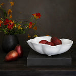 beatriz ball medium vida nube bowl with red fruits on a dark surface next to a vase of flowers.
