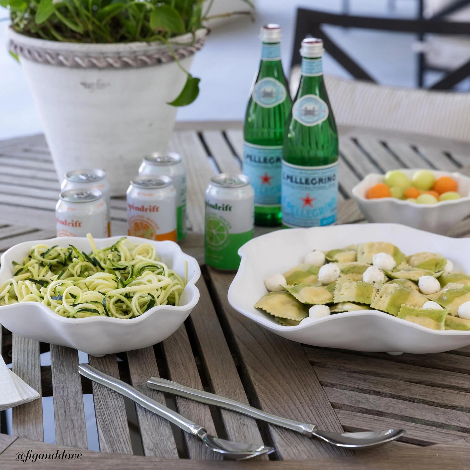 Two bowls of pasta with bottles and cans on a wooden table outdoors.