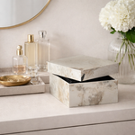Marble-patterned box on a vanity with decorative items including a vase of white flowers.