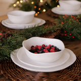 White bowl with berries on a white plate on a woven mat with Christmas decorations.