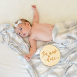 Newborn baby lying on a white blanket with a 'I'm new here' disc