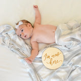 Newborn baby lying on a white blanket with a 'I'm new here' disc