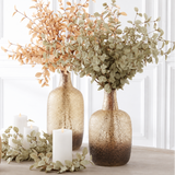 Three textured glass vase centers in a warm champagne-to-brown ombre finish, styled with dried botanicals and white candles on a light wood surface against a white paneled wall.