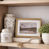 Decorative shelf with books, jars, a framed picture, and plants against a neutral wall.