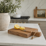Wooden cutting board with lemons on a kitchen counter, potted plant and stove in the background.