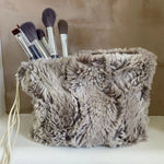 Fluffy gray pouch with makeup brushes on a neutral background