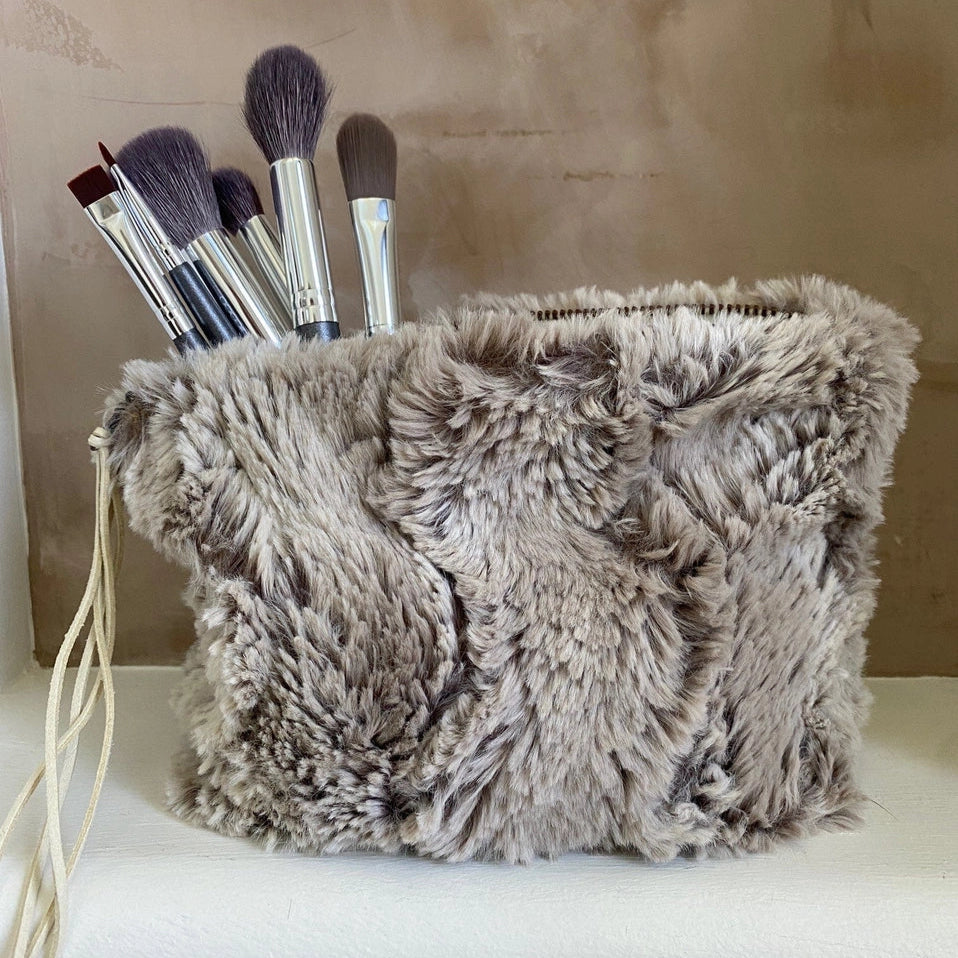 Fluffy gray pouch with makeup brushes on a neutral background