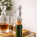 Wine bottle with a golf-themed cork stopper on a table with decanter and glasses.