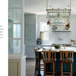 Modern kitchen with wooden island and chairs, white cabinets, and large windows.