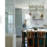 Modern kitchen with wooden island and chairs, white cabinets, and large windows.