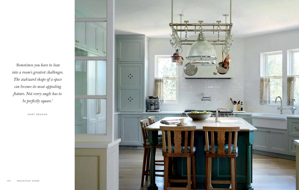 Modern kitchen with wooden island and chairs, white cabinets, and large windows.