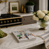 Kitchen counter with a book, bowl of artichokes, vase of white flowers, and decorative items.