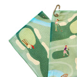 Golf-themed towel with golfers on a green background, folded and hanging.