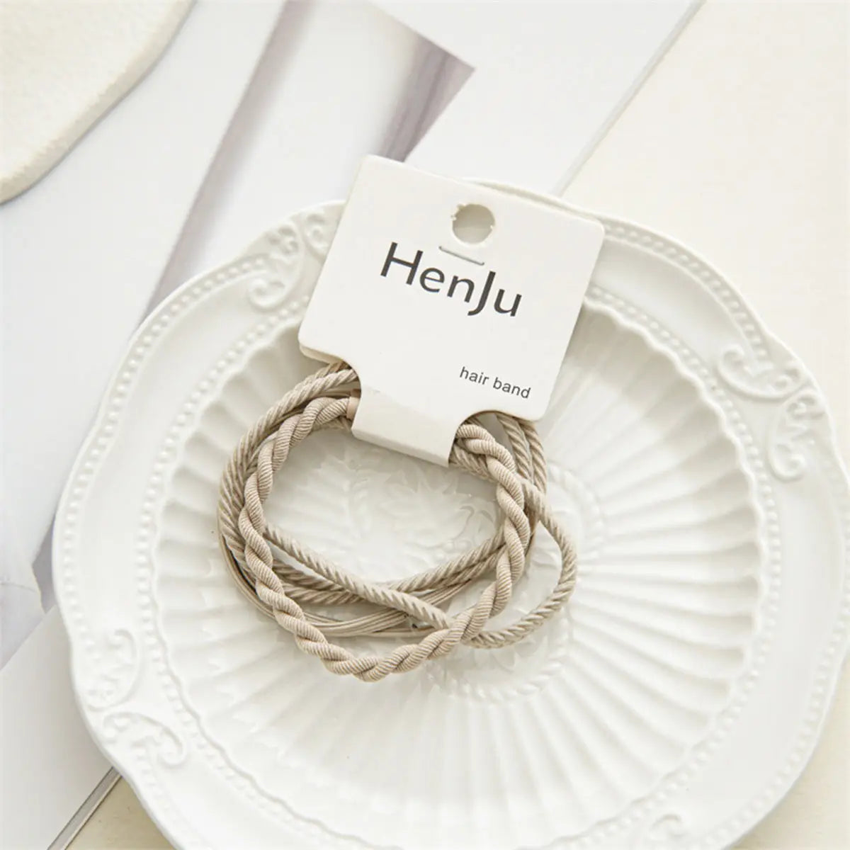 Beige hair bands on a white decorative plate with HenJu packaging.