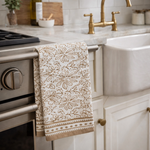 Patterned towel hanging on a kitchen cabinet handle with a sink and stove in the background.