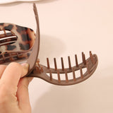 Brown hair clip with tortoiseshell pattern held by a hand against a beige background