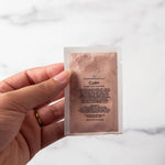 Hand holding a skincare product packet against a marble background