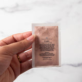 Hand holding a skincare product packet against a marble background