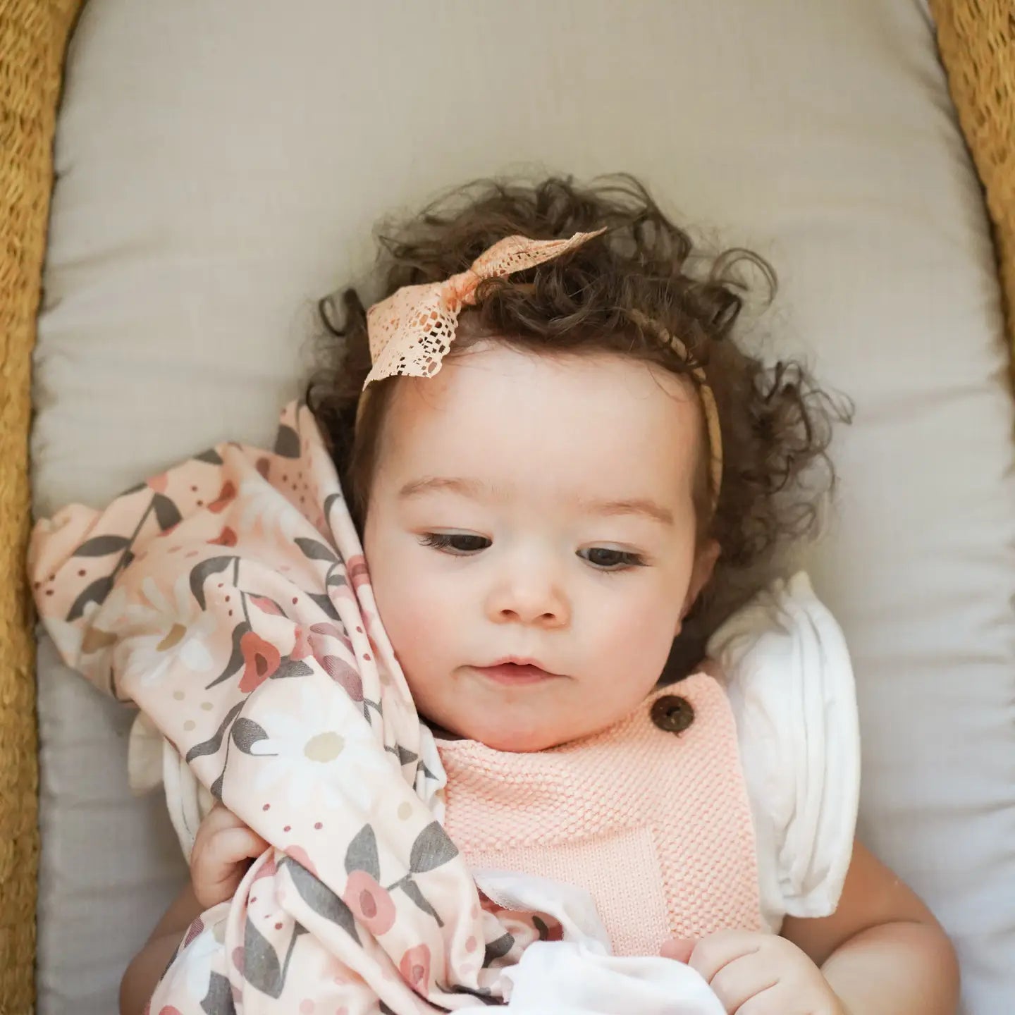Baby lying on a cushion with a floral blanket and headband