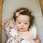 Baby lying on a cushion with a floral blanket and headband