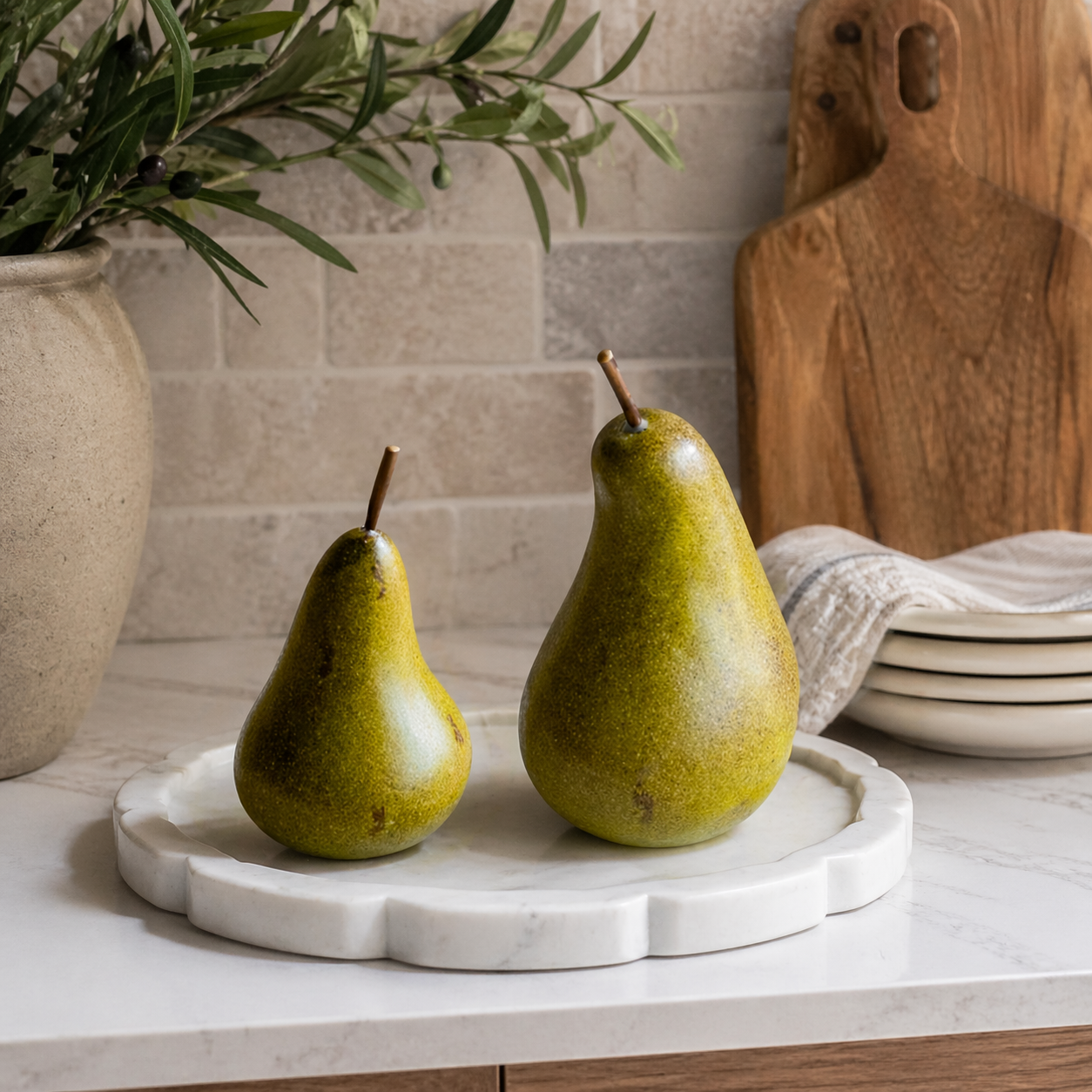 Two green pears on a marble tray with a kitchen setting in the background.