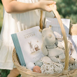 Child holding a Easter basket with a book, stuffed toy, and eggs.
