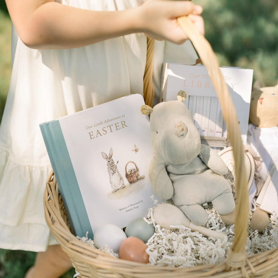 Child holding a Easter basket with a book, stuffed toy, and eggs.
