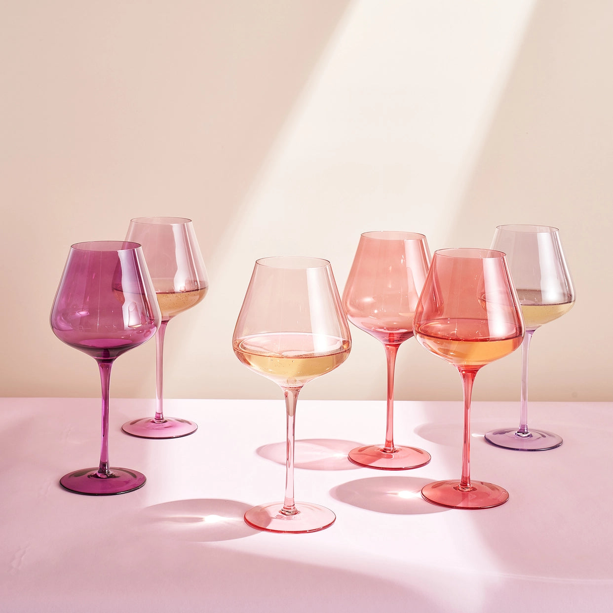 Set of six wine glasses with pink and purple hues on a light background