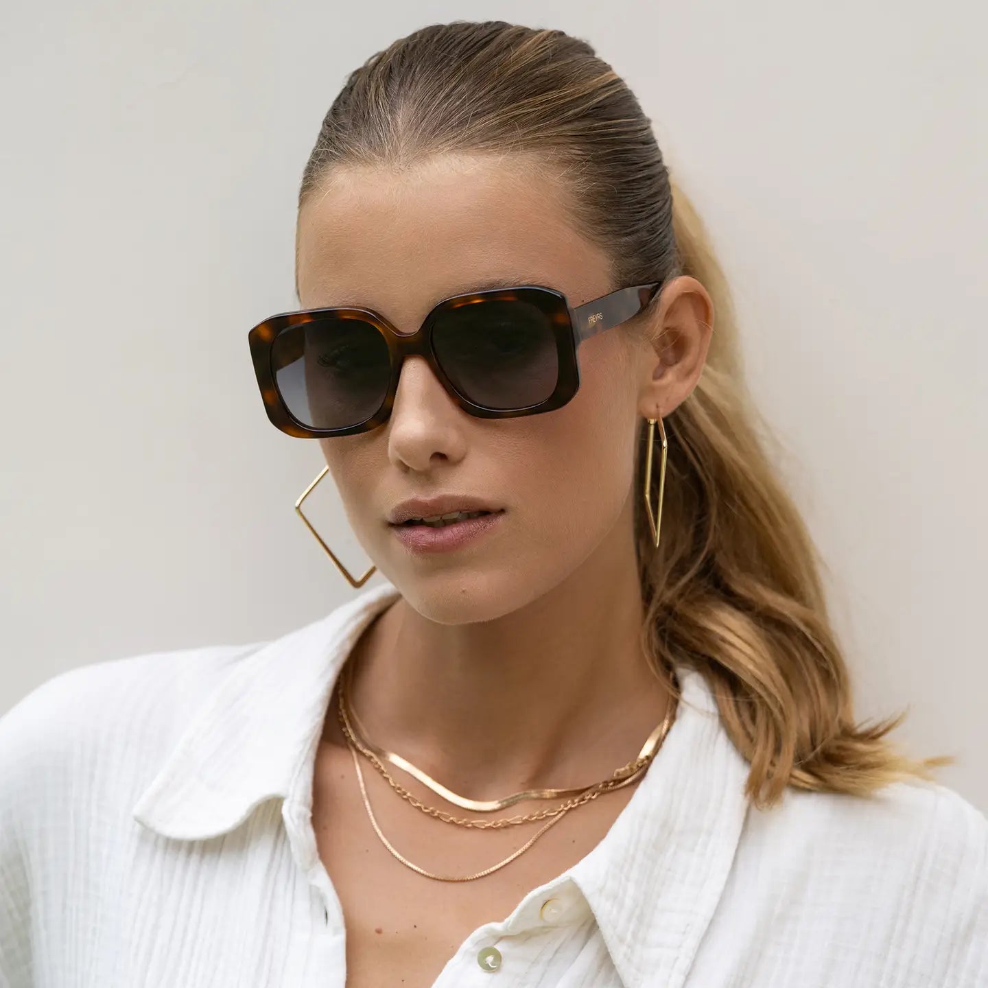 Woman wearing sunglasses and gold jewelry against a neutral background