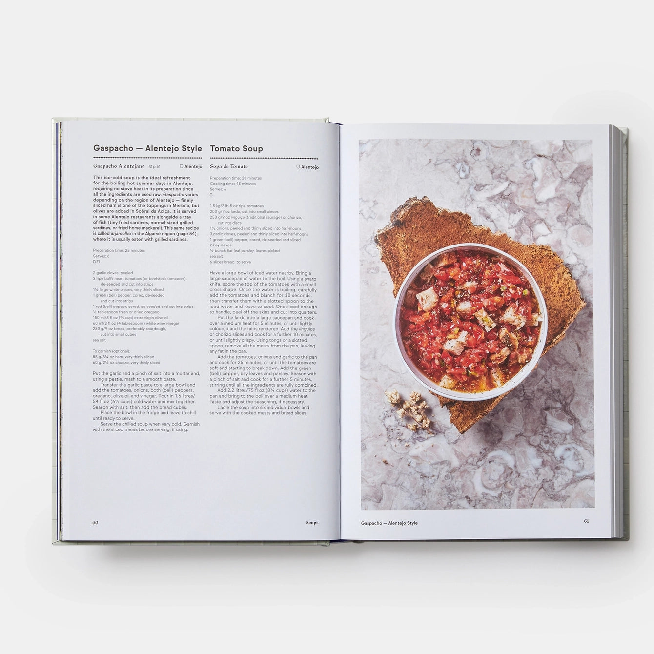 Open cookbook showing a recipe for Gazpacho with a bowl of soup on a marble surface.