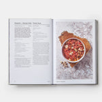 Open cookbook showing a recipe for Gazpacho with a bowl of soup on a marble surface.