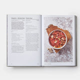 Open cookbook showing a recipe for Gazpacho with a bowl of soup on a marble surface.